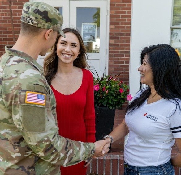 Red Cross volunteer stands on the front porch of a home shaking hands with a service member in uniform